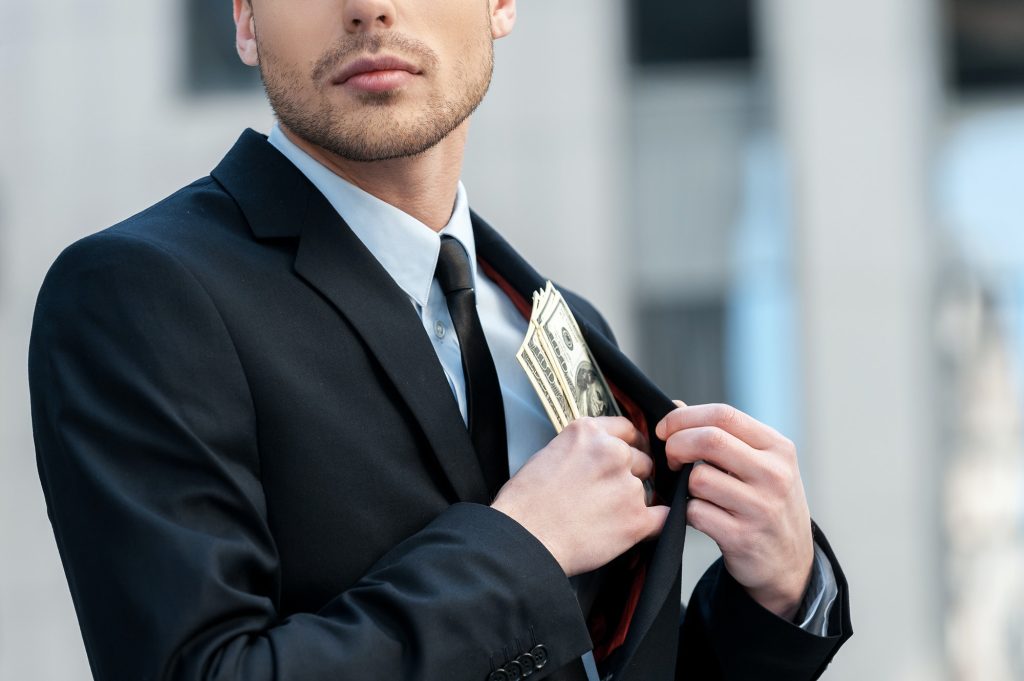 Pocketing company money. Cropped shot of a businessman placing money into his pocket